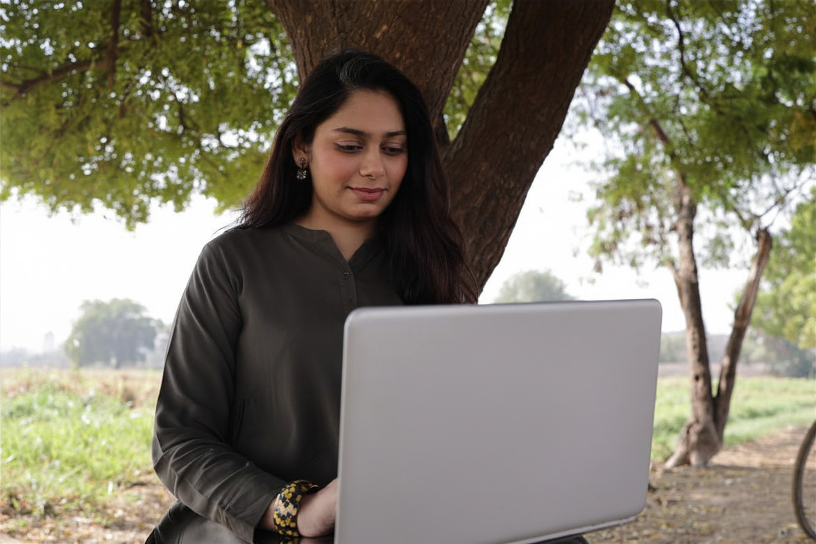 A woman working on a laptop outdoors under a tree