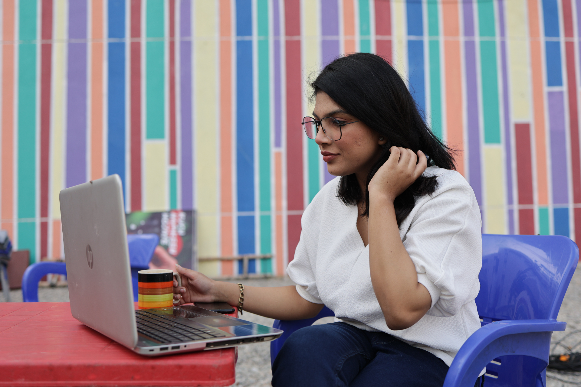 A woman working on a laptop at an outdoor table in front of a colourful striped wall